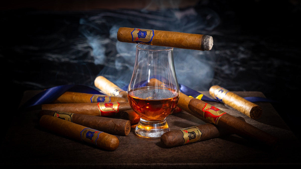 A cigar balanced on a glass of whisky, smoke curling above hand-rolled cigars on a dark table