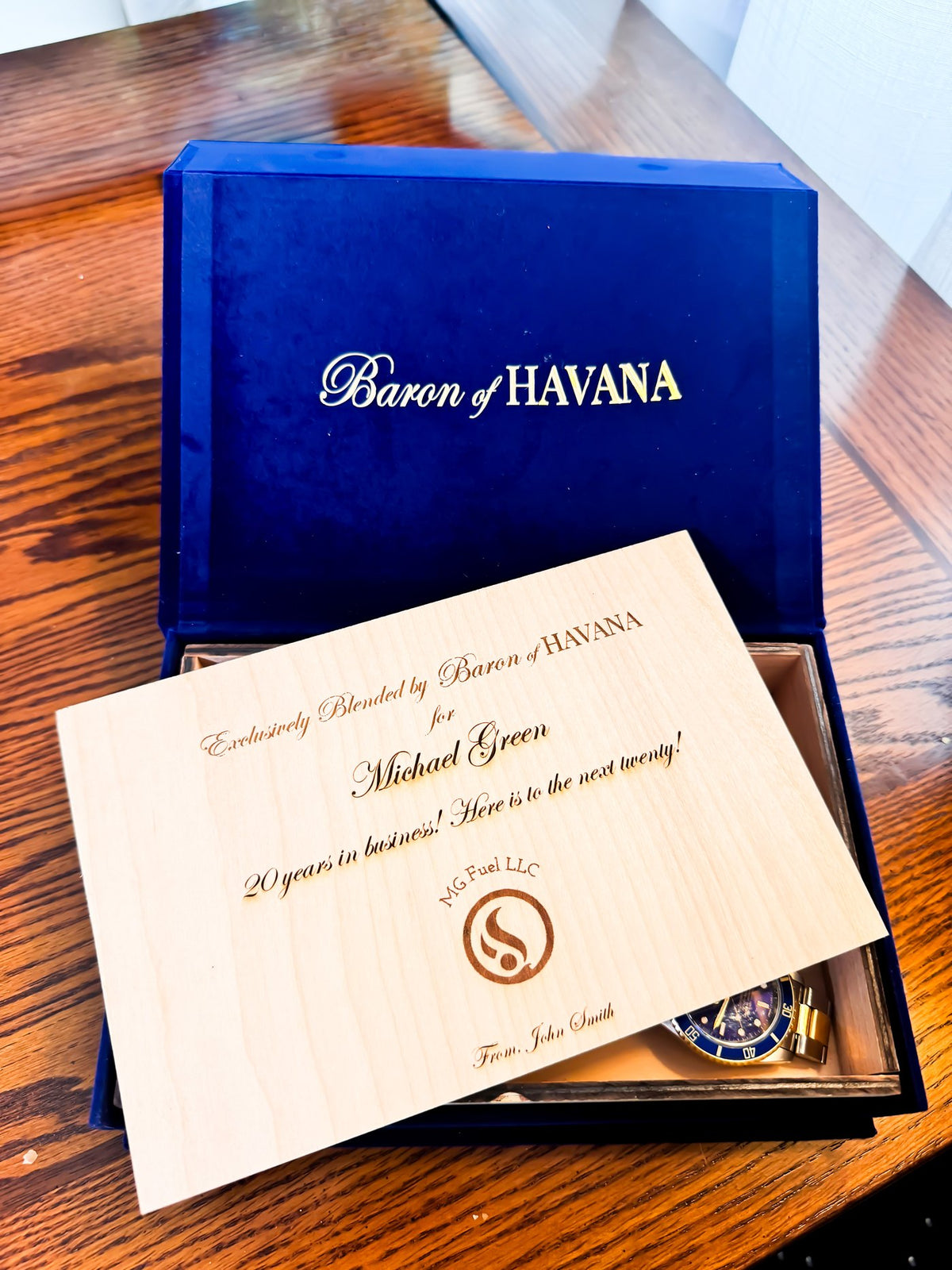 A personalized Baron of HAVANA box on a desk, its engraved cedar lid set aside to reveal a watch kept inside