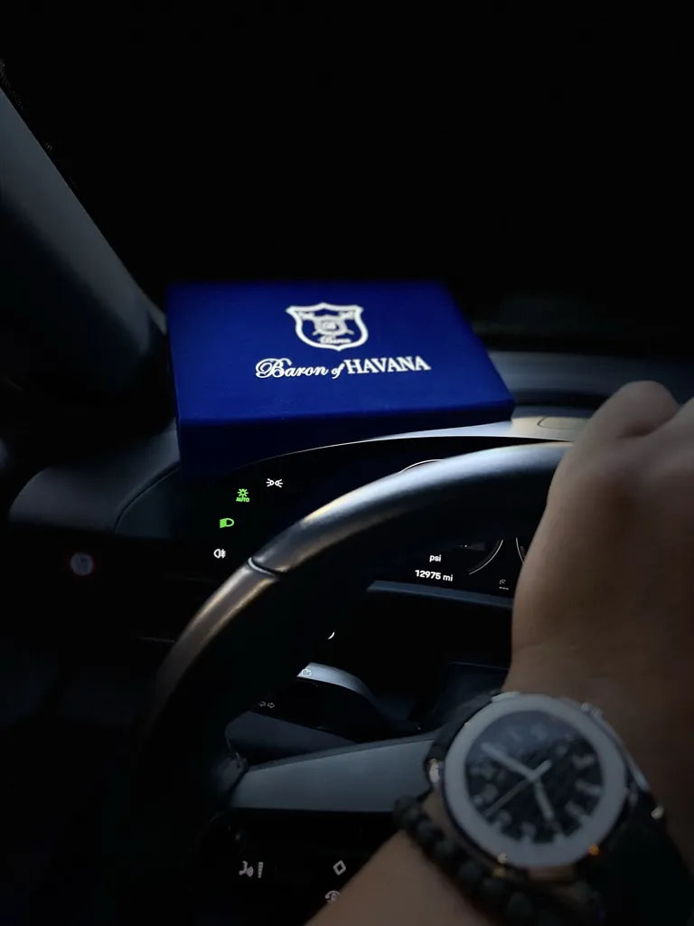 A Baron of HAVANA box on the dashboard of a car, beside a hand on the wheel